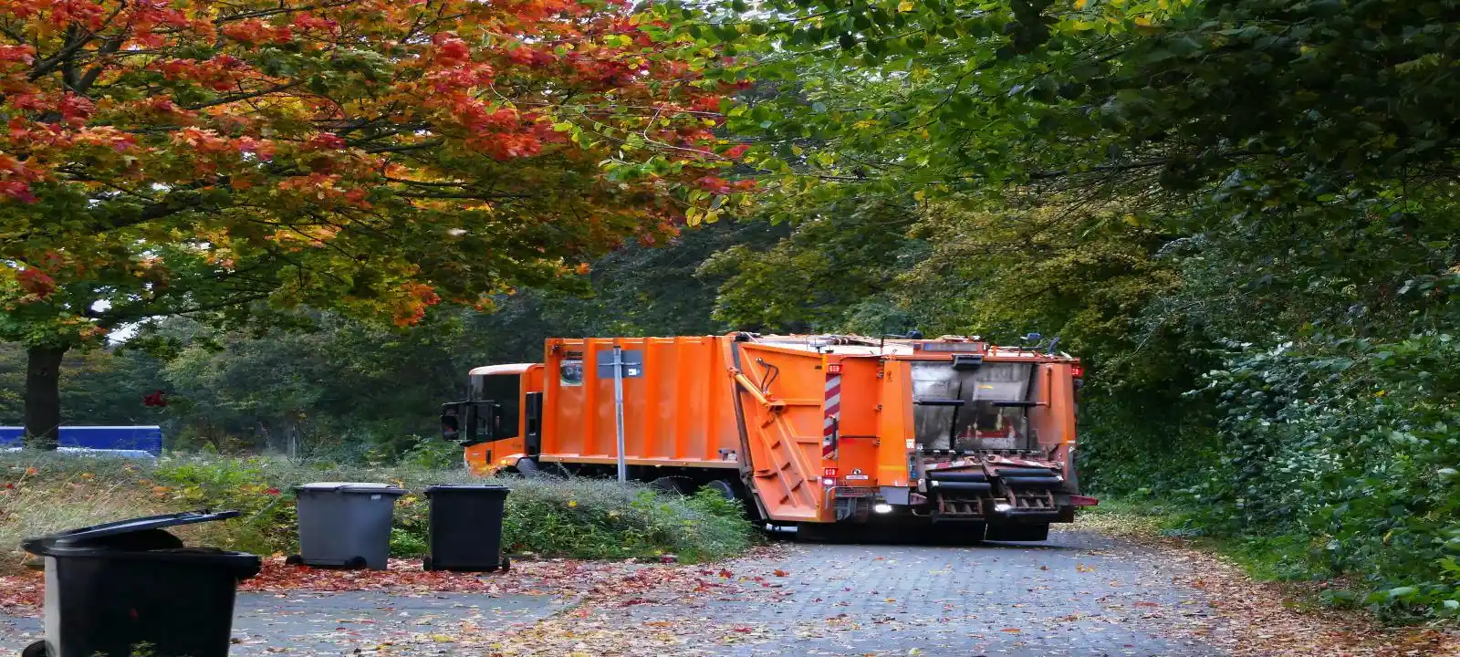 An orange skip bin loading truck servicing the area, collecting a full skip bin as part of skip bins townsville qld service